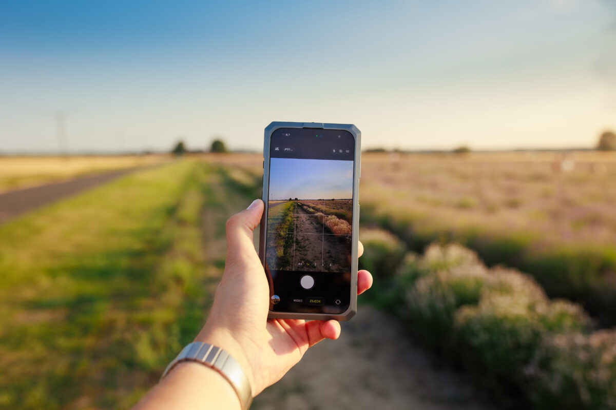 Dłoń trzymająca smartfon podczas fotografowania polnej drogi